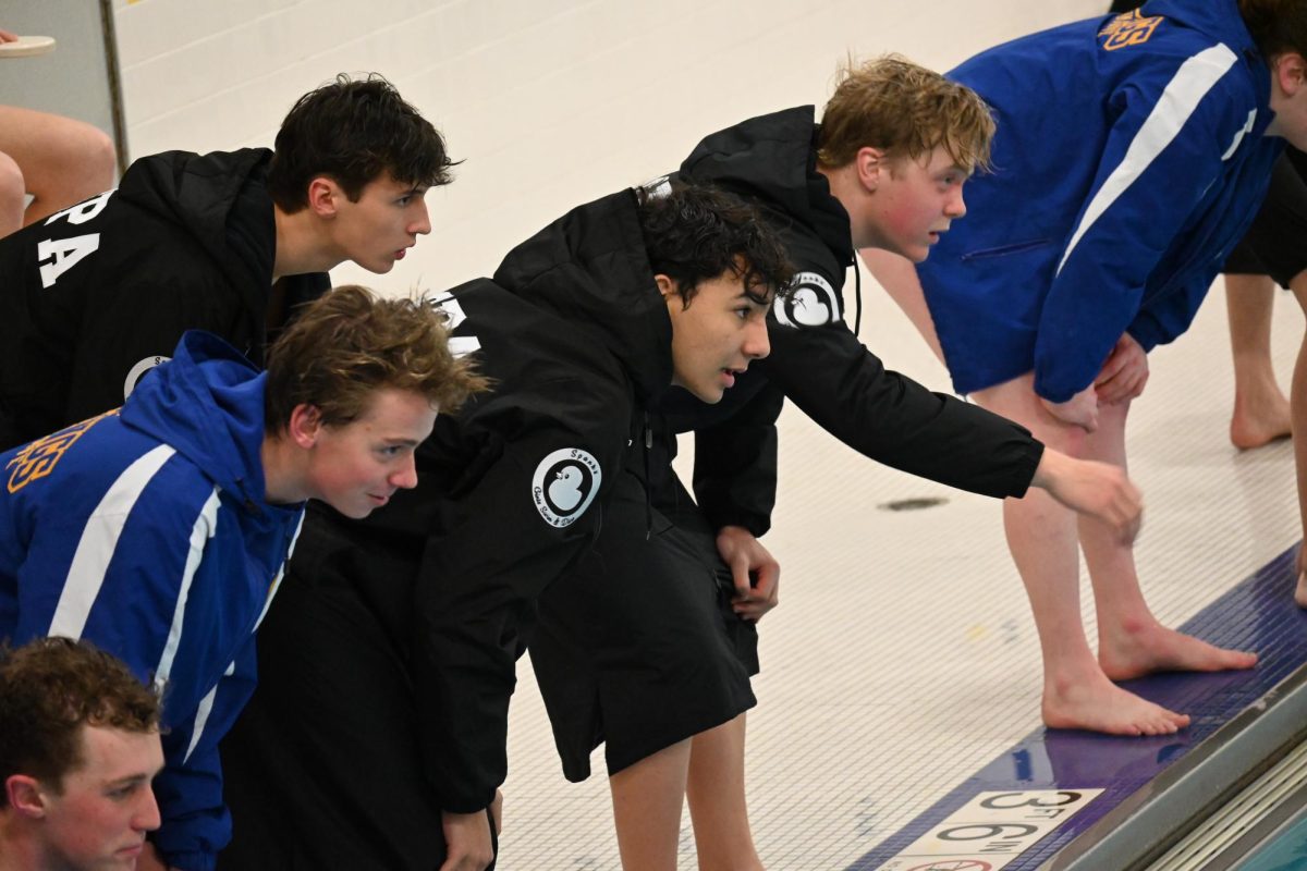 AMBITIOUS ANTICIPATION. A group of Trojan swimmers intently watch the 100 breaststroke.