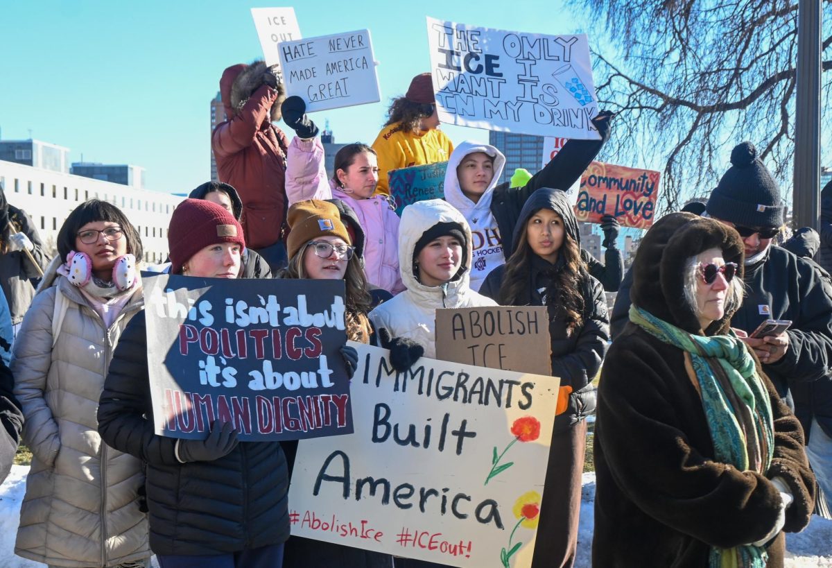 STAND TOGETHER. St. Paul students stand on the outskirts of the crowd, holding up signs and listening to the speakers.