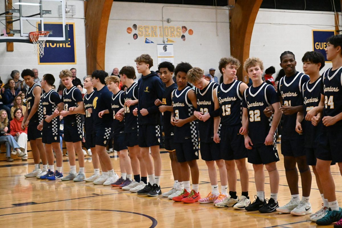 WITH THE WHOLE TEAM. Varsity, JV and C team players link arms for the national anthem. In a show of support for the younger players, the varsity team invited JV and C team players to sit on the bench and join the line for the national anthem.