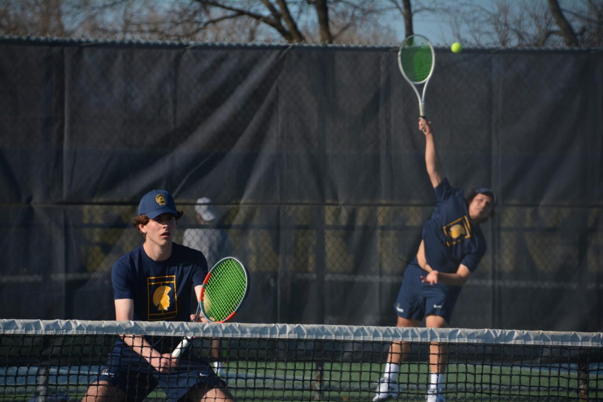 DOUBLES DOMINANCE. Captain Isaak Senaratna fully extends for a powerful serve while sophomore Henry Cammack maintains a ready stance at the net. The No. 1 doubles pair utilized this "serve-and-volley" pressure to keep their Edina opponents off-balance throughout the set.
