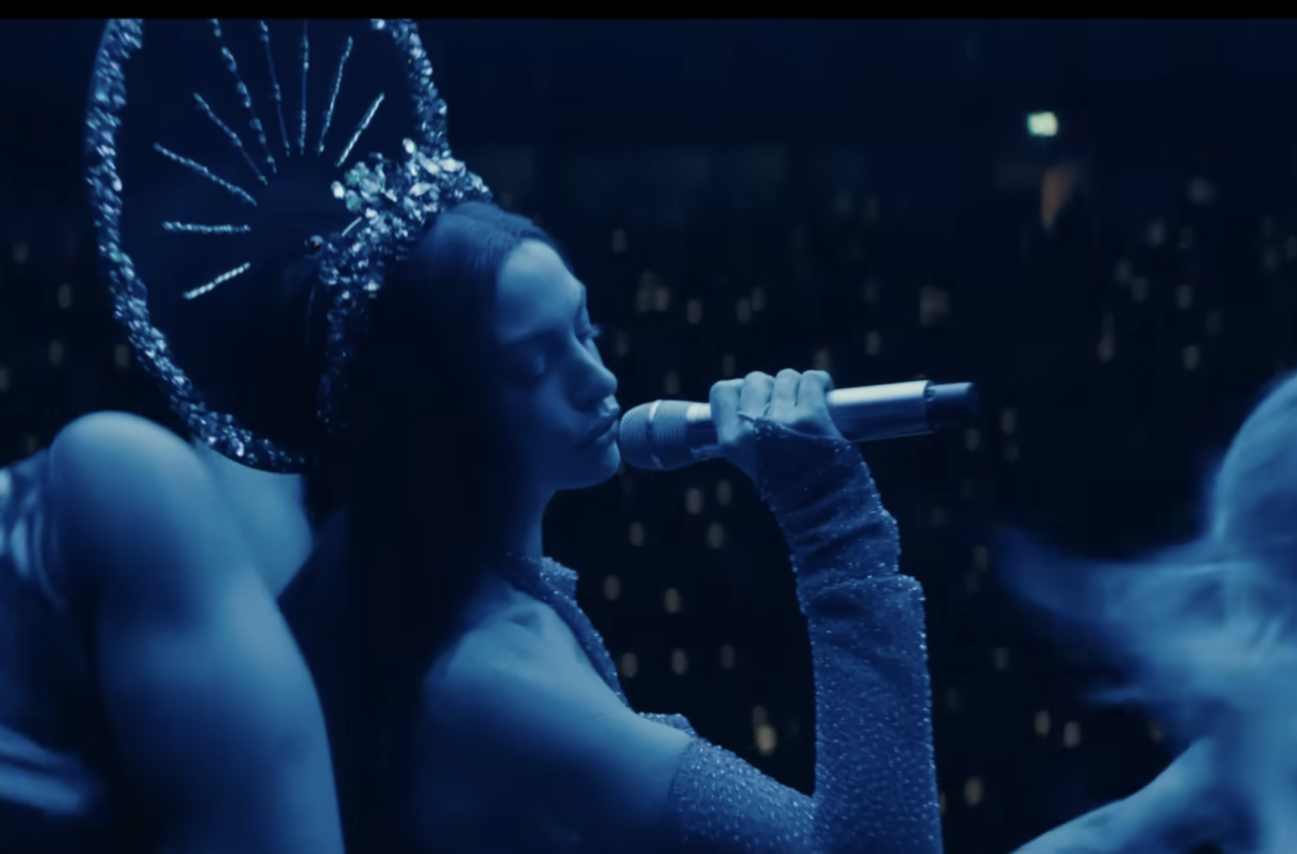 MEGASTAR MOMENT. Anne Hathaway performs in "Mother Mary." The concert scenes are astonishing, shot on location at a massive arena in Western Germany, and the scale is tremendous. Christ-like images are littered throughout the performance scenes, and Lowery used Taylor Swift’s “Reputation” Stadium Tour as a key visual guide. (Fair Use: A24 movie trailer)