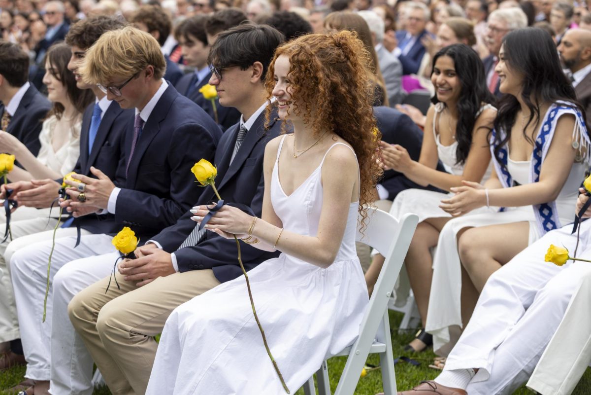 EXCITED AUDIENCE. The class of 2025 applauds during the 2025 commencement ceremony on the front lawn of the school grounds. Traditional graduation attire includes long white dresses and navy blazers. Assistant Principal of Student Life Stacy Tepp said, “There used to be a bouquet that female students would carry, and that went away … now everyone gets a single yellow rose.” 